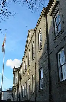 Photo de la façade d'un bâtiment en pierre beige portant les armoiries des États de Guernesey