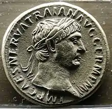 pièce de monnaie en métal gris, présentant un jeune homme de profil aux cheveux ceints d'une couronne de laurier, entouré d'inscriptions.
