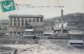 Un haut bâtiment maçonné à quatre étages entouré de bâtiment plus petits.