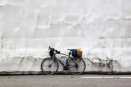 Un vélo appuyé contre l'un des « murs » de neige bordant la route à la fin du printemps, après le déneigement de celle-ci.