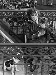 Photo en noir et blanc, prise sur un balcon fleuri, d'une femme entre deux âges tenant un chat dans ses bras
