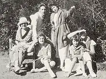 Photographie en noir et blanc montrant Colette, sa fille et quatre de ses amis dans un jardin ensoleillé. L’environnement paraît champêtre.