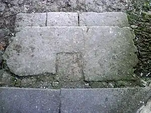 Photographie en couleurs d'une pierre rectangulaire portant une échancrure carrée en son centre.