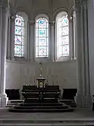Photographie en couleurs du chœur d'une église : trois vitraux éclairent l'autel.