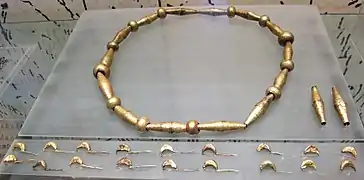 18 fibules et un collier en or composé de 12 boules en enfilade, alternant avec 14 cônes et 2 supplémentaires sur le côté.