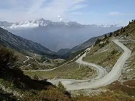 Photographie en contre-plongée d'un col de haute montagne par beau temps, avec une route serpentant à flanc de colline. En arrière-plan, une chaîne de montagnes.