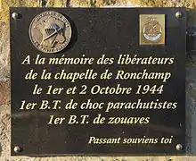 Plaque de marbre portant deux écussons et les inscriptions : À la mémoire des libérateurs de la chapelle de Ronchamp le 1er et le 2 octobre 1944, 1er BT de choc parachutistes et 1er BT de zouaves. Passant souviens toi.