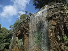 Vue de trois-quarts d'une cascade de quelques mètres de hauteur et de largeur dans un parc sous un ciel bleu.