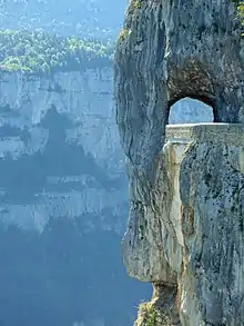 Une route à flanc de précipice passe sous une arche dans la roche.