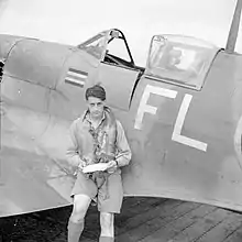 Photo noir et blanc. Colin Gray est adossé au fuselage de son appareil et tient des feuilles dans sa main.