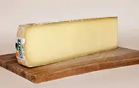 photo couleur d'une tranche de fromage couleur ivoire sur une planche en bois. La morge est plus sombre.