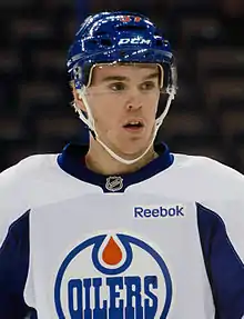 Photographie d'un joueur de hockey avec un maillot blanc et un casque bleu