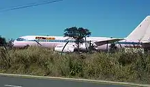 Cliché numérique couleur. Profil d'un avion à réaction paraissant dans un terrain vague envahi d'herbes.