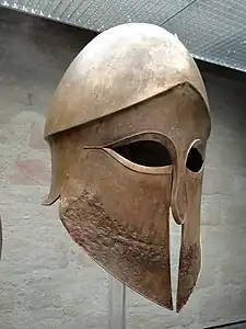 Casque corinthien issu de la tombe d'un dénommé Denda. Le nom du guerrier est gravé sur la cnémide gauche elle aussi déposée dans la sépulture. Provient d'un atelier grec d'Italie du Sud, 500-490 av. J.-C.