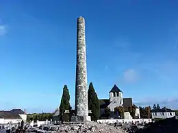 Photographie représentant un cimetière, colonne au premier plan et église en arrière-plan.