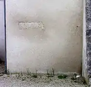 Photographie en couleurs d'un linteau en pierre isolé sur un mur crépi.
