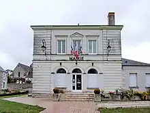 Photographie en couleurs d'un bâtiment portant le mot « mairie » et des drapeaux sur sa façade.