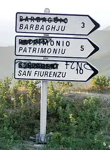 Panneau de signalisation bilingue français et corse dont les toponymes français ont été effacés par graffiti