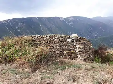 Vue depuis une colline au nord de Conat, près de Santa Margarita, en regardant vers le sud. L'ancien "cortal" au premier plan a été construit avec du schiste cambrien du coin. À l'arrière-plan se dressent des falaises de calcaire du Dévonien, qui dominent la vallée du Caillan.