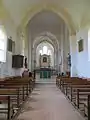 Nef à une travée aux murs blancs vue depuis l'entrée, une chaire en bois suspendue au mur de gauche, voûtes en ogive, deux statues de part et d'autre du transept