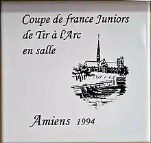 Photo d'un carreau de faïence avec un dessin au trait de la cathédrale d'Amiens, avec l'inscription coupe de France juniors de tir à l'arc en salle, Amiens 1994.