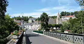 Photographie en couleurs d'un village au flanc d'un coteau avec un pont au premier plan.