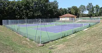 Deux courts tennis dont l'aire de jeux est colorée en violet et l'extérieur est en vert. En fond se trouve un bâtiment jaune qui fait office de club-house