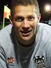 photo en tronc d'un homme souriant aux cheveux courts portant un maillot gris