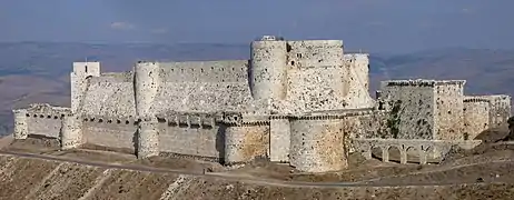 Photographie d'un imposant château fort composé de deux rangées de murailles situé dans un paysage valonné recouvert de maquis