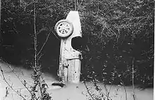 Photo d'une voiture accidentée, le nez, enfoncé dans un cours d'eau, à la verticale.