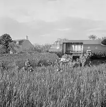 Photo noir et blanc de soldats en tenue de combat près d'un planeur enfoncé dans un muret.