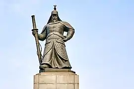 Photographie d'une statue d'homme en armure du Moyen Âge coréen, portant une grande épée dans sa main droite.