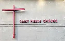 Croix rouge et inscription "Saint Pierre Chanel" en rouge, sur un mur en béton.