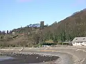 Photographie d'un coteau boisé surmonté d'un clocher et dominant un estuaire.