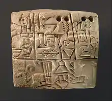 Tablette en argile divisée en cases comprenant des signes proto-cunéiformes et numériques, et une impression de sceau-cylindre partiellement visible.
