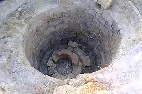 Trou dans le sol supporté par des briques circulaires. Au fond du trou, plusieurs briques sont entreposées.
