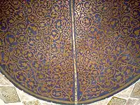Photographie de la demi-coupole du mihrab. Son décor peint, de couleur jaune sur fond bleu nuit, est établi de façon symétrique et se compose de rinceaux et de motifs végétaux stylisés.