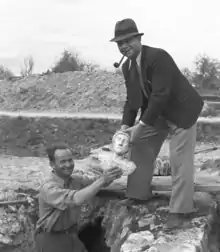 Photo en noir et blanc de deux hommes tenant une statuette au-dessus d'un trou.