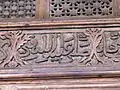 Détail d'une inscription arabe en style naskhi. Elle est sculptée en relief sur la traverse située au-dessous du tympan de la grande porte de la salle de prière.
