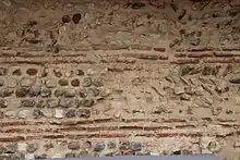 Détail d'un mur en pierres de différentes couleurs avec des rangs de briques.