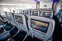 Photo couleur de l'intérieur d'une cabine passagers d'un avion de ligne vue au-dessus des sièges. Elle montre les rangées centrales de quatre sièges, avec des écrans incorporés sur chaque dossier.