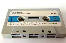 Une cassette grise avec une étiquette blanche et bleu clair.