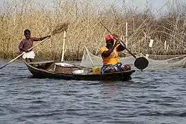 Femme et son enfant dans une pirogue, naviguant devant un acadja