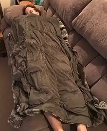 Une femme allongée sur un canapé, sous une couverture qui semble épaisse et qui la recouvre de son nez aux chevilles.