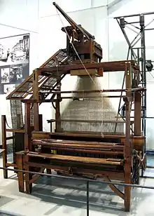 Un vaste métier à tisser en bois, tendu de fils, est installé dans une salle d'exposition.