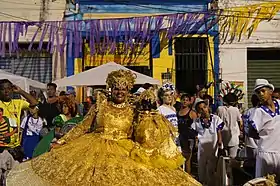 Une dame du palais du maracatu Encanto de Alegria portant sa calunga devant la casa das tias.