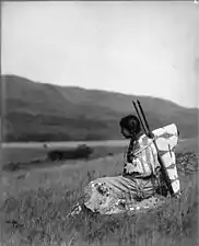 Daisy Norris, pikunie, portant un porte-bébé sur planche avec un nourrisson dedans, Parc national de Glacier, Montana