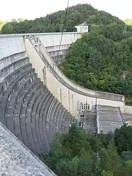 Un barrage est pris en photo depuis le côté en haut. C'est le côté opposé à la retenue d'eau, vers la vallée avec des arbres.