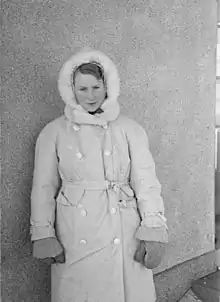 Une jeune femme souriante emmitouflée dans un épais manteau.