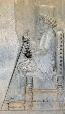 Photo d'un bas-relief représentant un personnage de profil aux cheveux et à la barbe bouclés assis sur un trône.